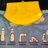 Yellow plastic device with diagrams of Islamic prayer positions on a blue fabric background