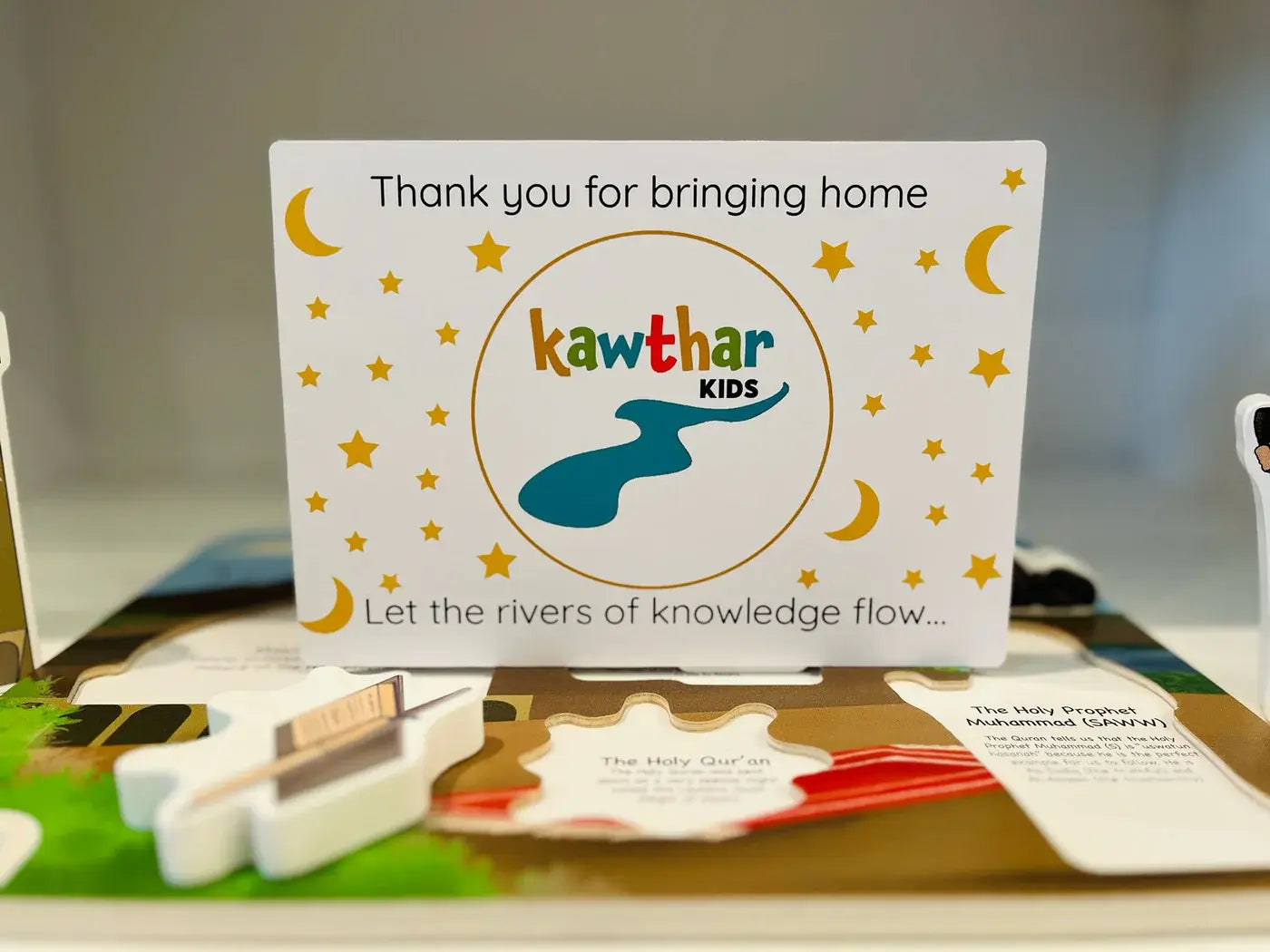 Card with 'Kawthar Kids' branding on a table with educational materials.