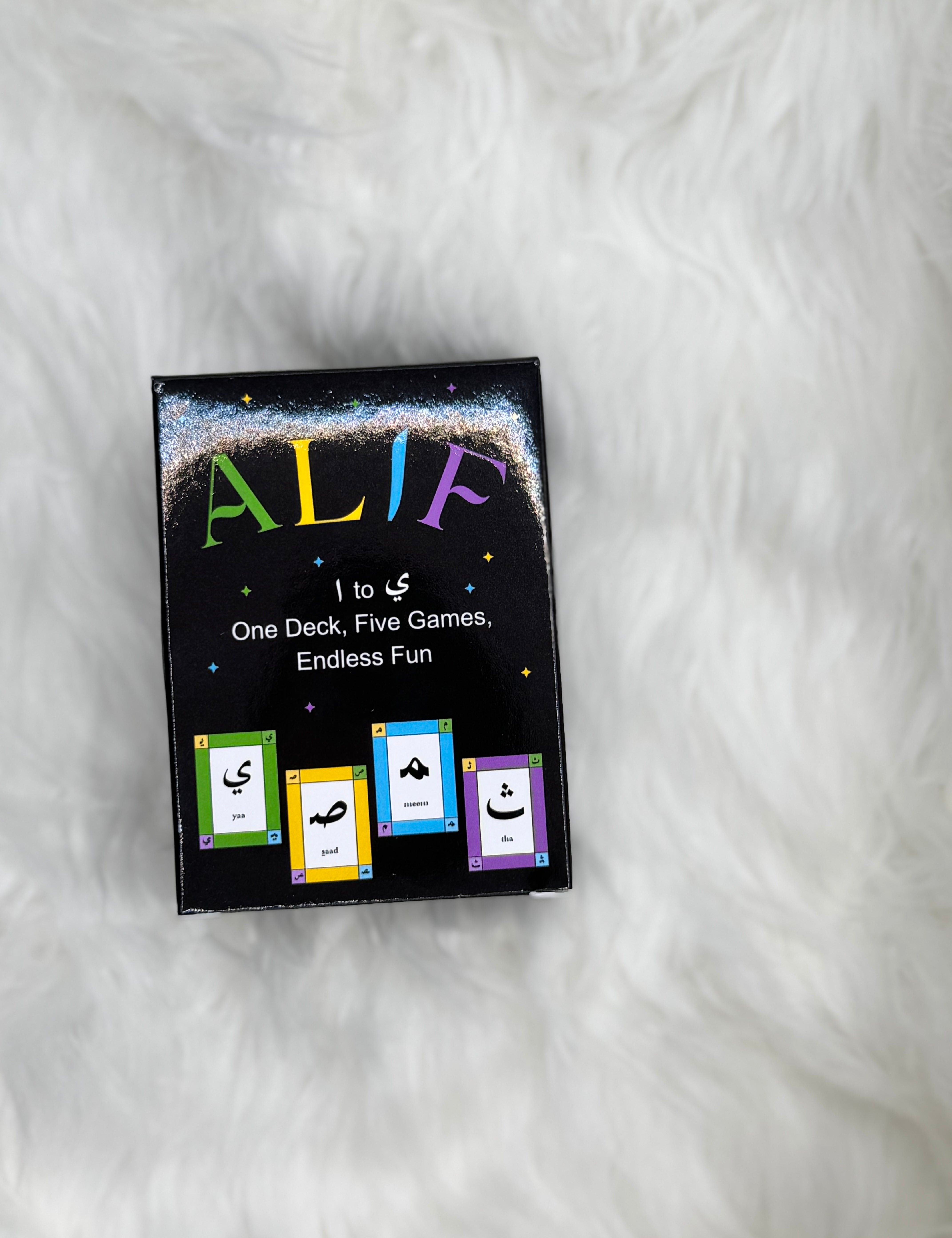 Card game box labeled 'ALIF' on a white fur background