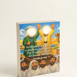 A small rectangular printed card or booklet standing upright on a white surface against a white background. The front shows an illustrated scene with people in traditional clothing and Arabic and English text.