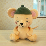 A plush toy mouse sitting on a light wooden table, wearing a dark green beret-style hat. The toy has a warm beige body, pink inner ears, closed embroidered eyes, and a small orange-brown backpack, set against a patterned wallpaper background.