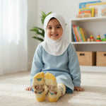 A young child wearing a light blue modest outfit, white hijab, and Aliya and Hasan Bookshelf yellow socks sits smiling on a cream rug in a bright, modern playroom.