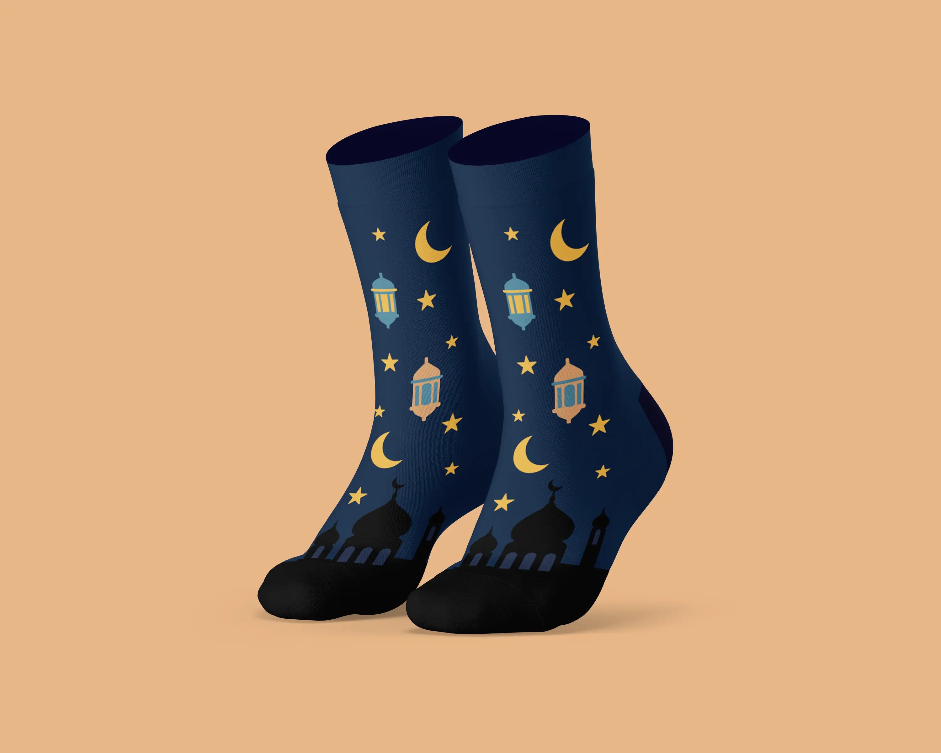 A pair of dark navy blue crew socks with a festive Ramadan pattern featuring yellow crescent moons, stars, lanterns, and mosque silhouettes, displayed against a solid peach background.