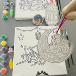 Canvas with crescent moon and star design, paint bottles, and brushes on a gray surface.