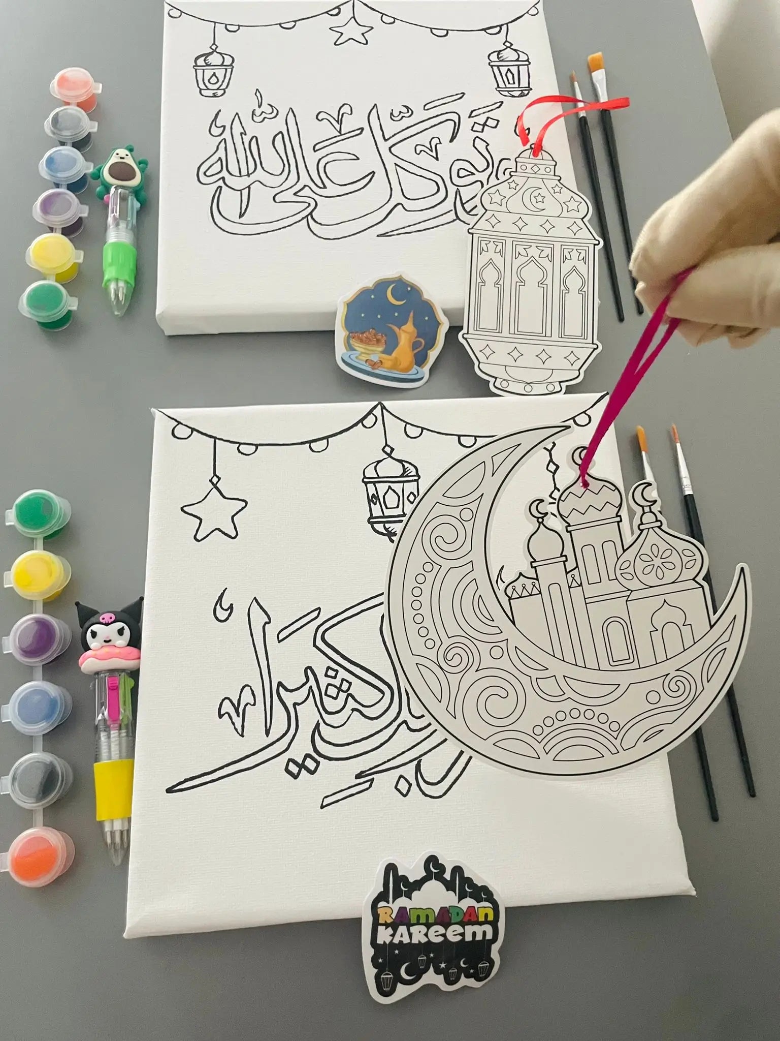 Canvas with crescent moon and star design, paint bottles, and brushes on a gray surface.