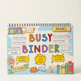 A colourful spiral-bound children's activity binder titled 'BUSY BINDER' with the name 'ABABEL' printed on the cover, photographed against a plain light beige background.