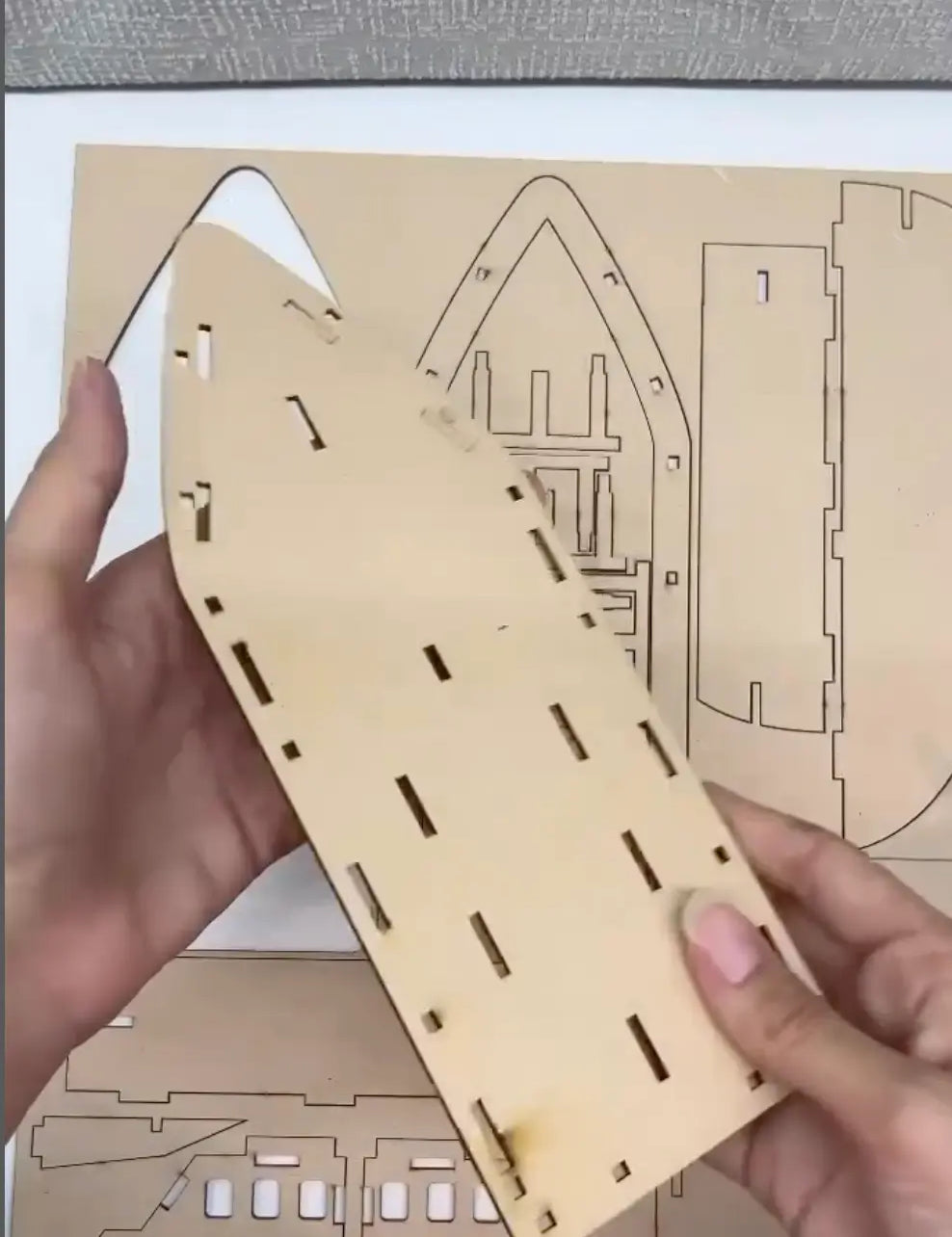 Wooden laser-cut puzzle piece held by hands with a detailed diagram in the background.