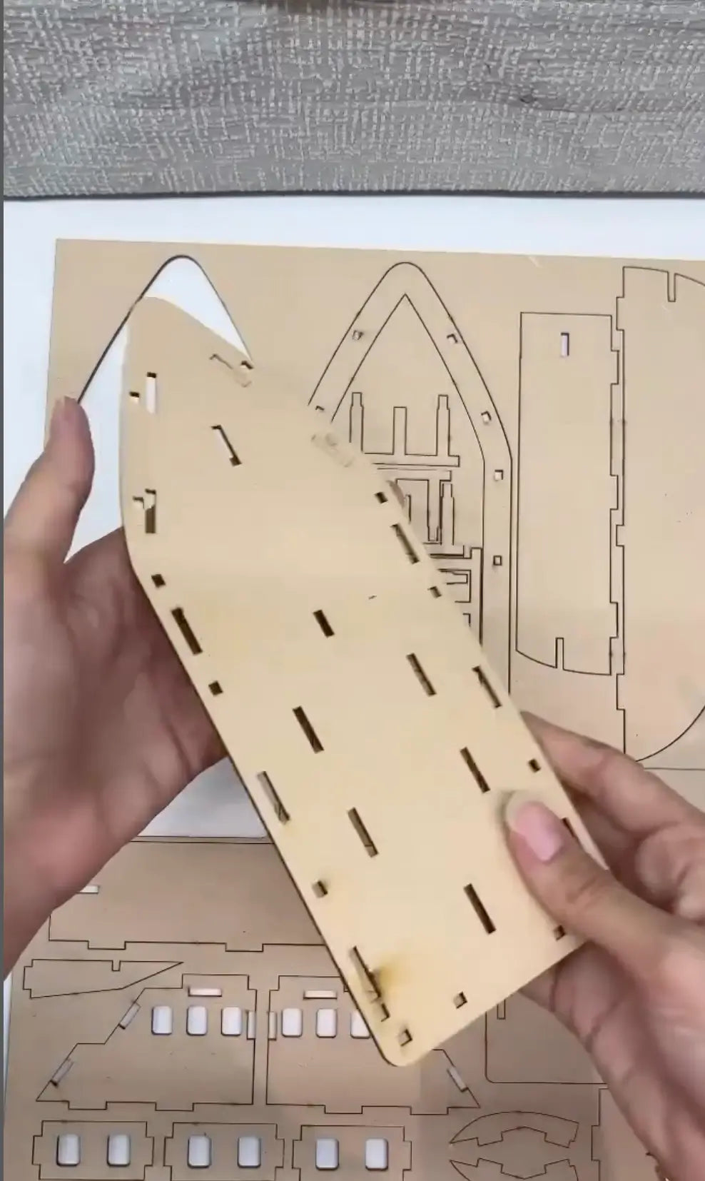 Wooden laser-cut puzzle piece held by hands with a detailed diagram in the background.