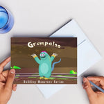 Book with 'Grumpaloo' design held by a hand on a light gray background