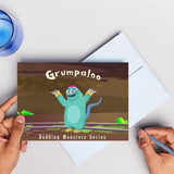 Book with 'Grumpaloo' design held by a hand on a light gray background