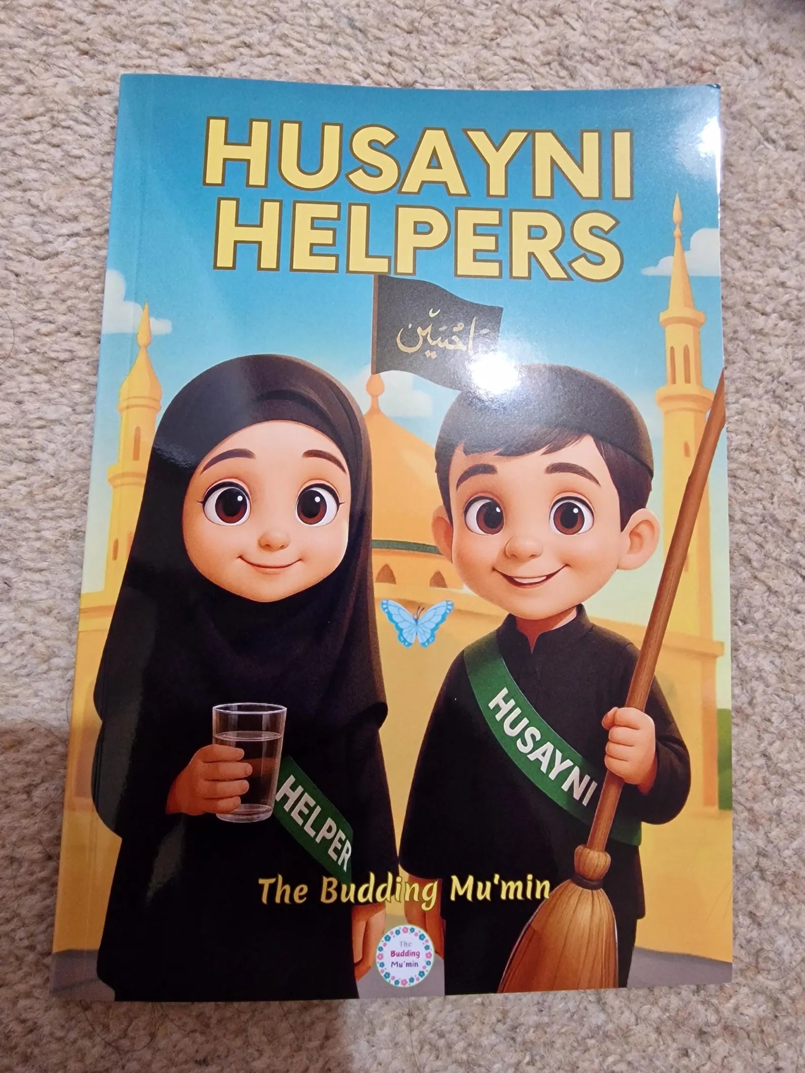 Book titled 'Husayni Helpers' with cartoon characters on a carpeted floor.