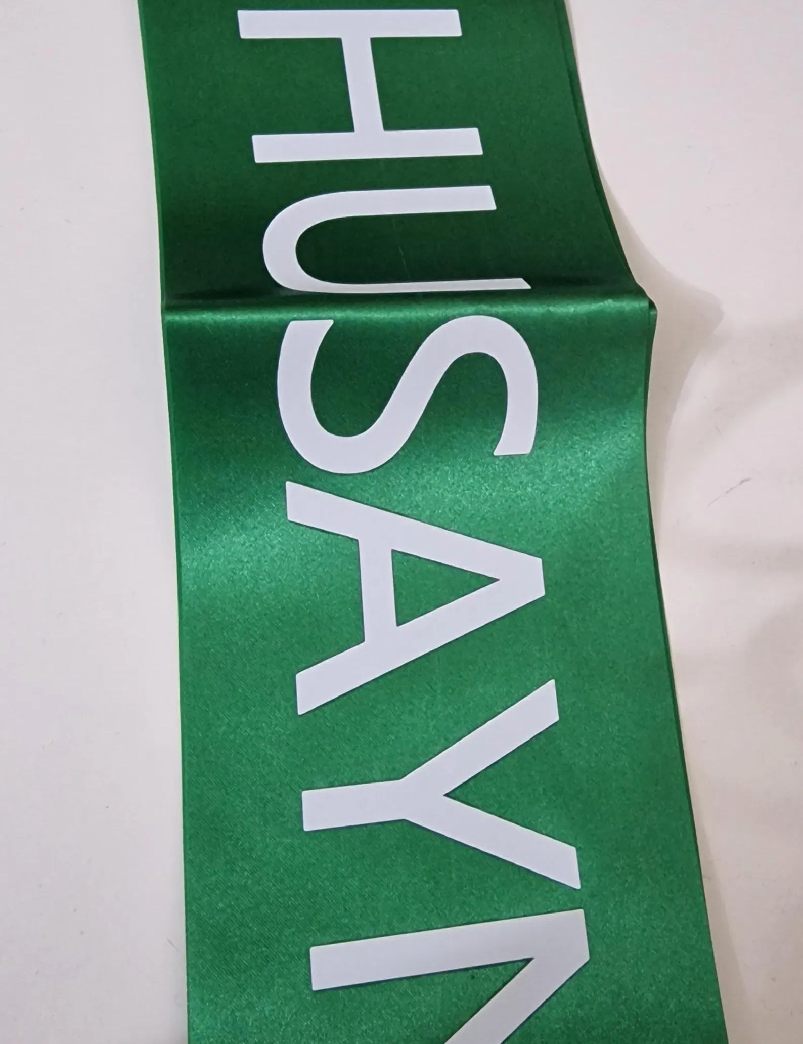 Green sash with 'HUSAYNI' printed in white on a white background