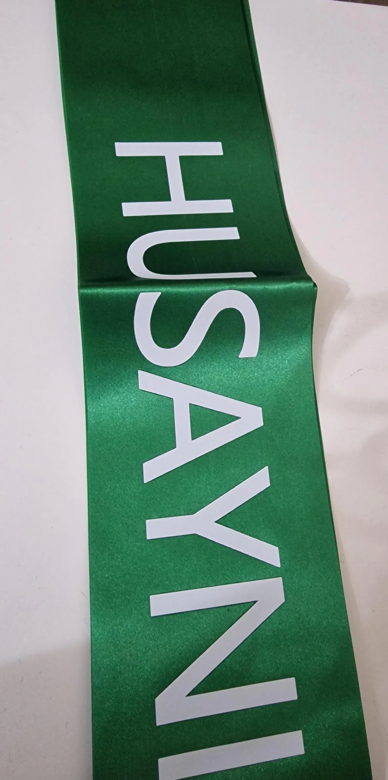 Green sash with 'HUSAYNI' printed in white on a white background