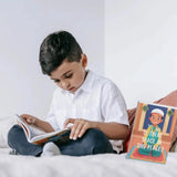 Child reading a book on a bed with a pillow featuring a cartoon character.