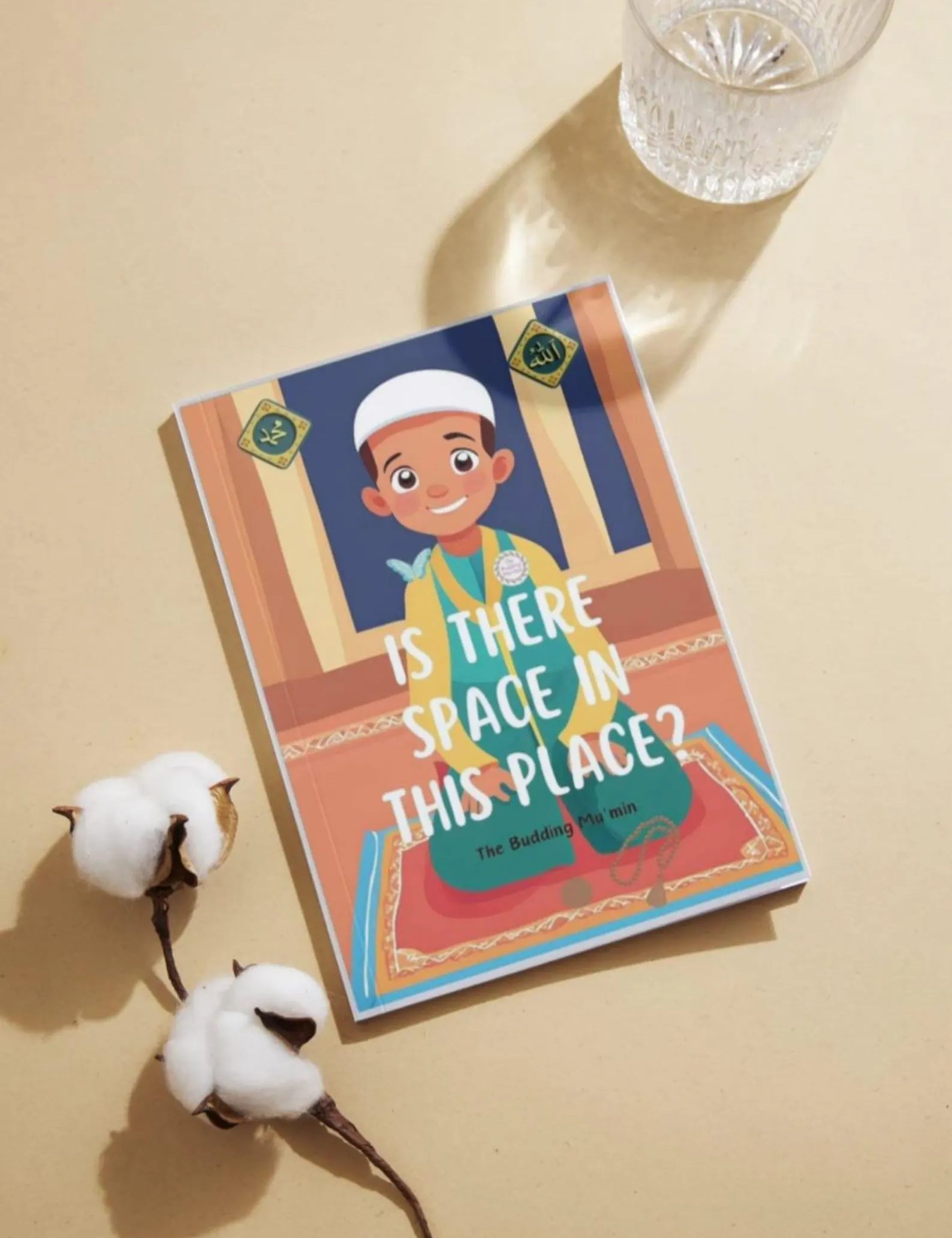 Book titled 'Is There Space in This Place?' By Budding Mumin on a beige surface with cotton and a glass of water.