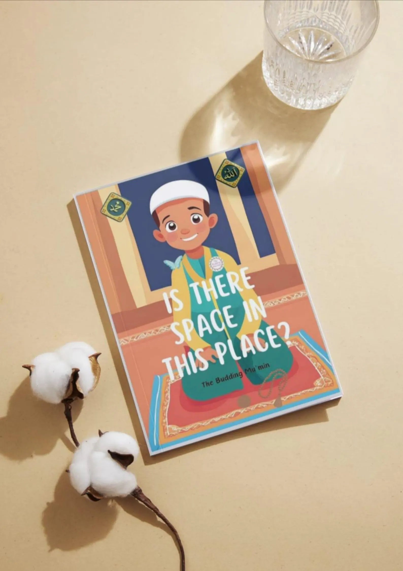 Book titled 'Is There Space in This Place?' By Budding Mumin on a beige surface with cotton and a glass of water.