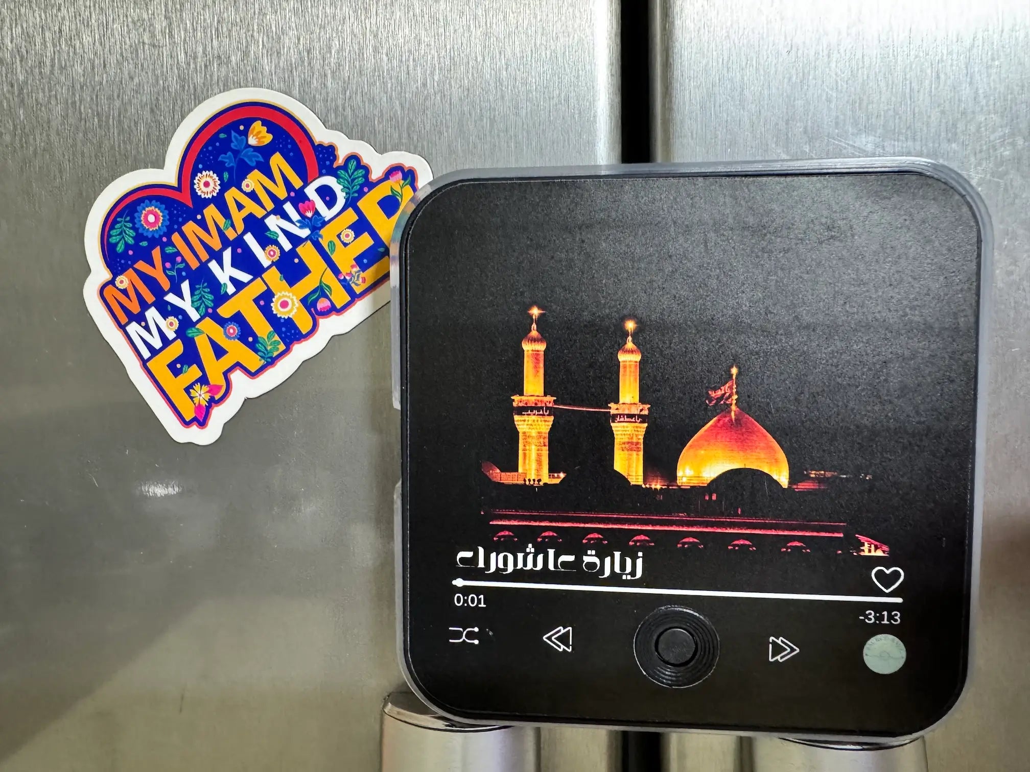 Phone with a dua ziyarat fridge magnet audio on a metallic surface next to a colorful sticker.